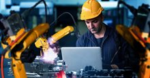 Construction worker working behind a laptop with a robot next to him, wearing work clothes and a helmet