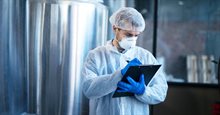 Industrial worker writing on a notepad and wearing a face mask, hairnet, gloves and protective jacket