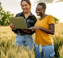 Twee vrouwen bekijken iets op een laptop in een weiland