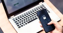 cybersecurity uitgebeeld met laptop op de achtergrond en telefoon met inlogcode op de voorgrond
