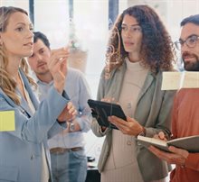 A meeting between men and women taking notes on a transparent glass using a marker.