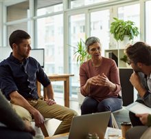 Company meeting of group sitting in a circle on chairs with laptops and tablets in hand